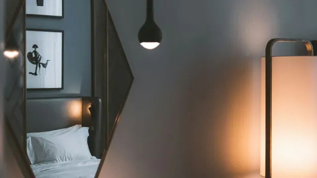 Gedämpft beleuchtetes Hotelzimmer mit Stehlampe und Bett im Spiegel