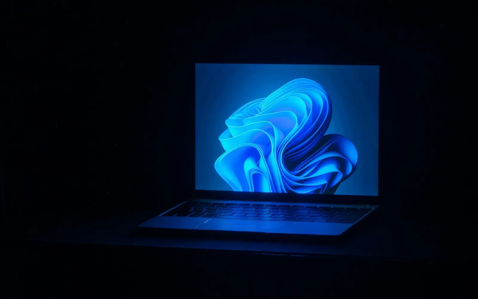 Laptop mit blau leuchtendem Bildschirm in einem dunklen Raum