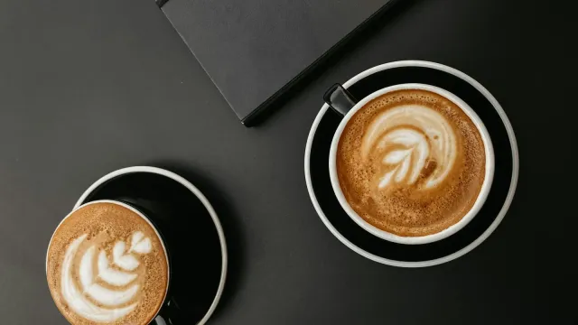 Zwei Cappuccino-Tassen und ein Notizbuch auf einem dunklen Tisch – Sie sucht Ihn Anzeigen im Vergleich